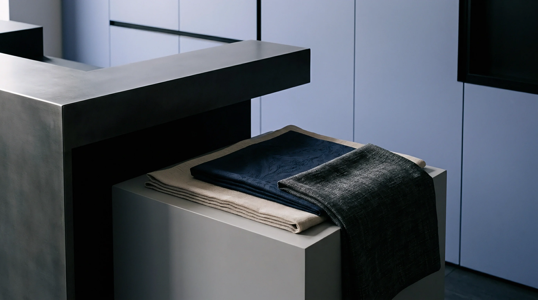 Layered woven textile pieces rest neatly upon a concrete grey display pedestal positioned inside a contemporary production studio.