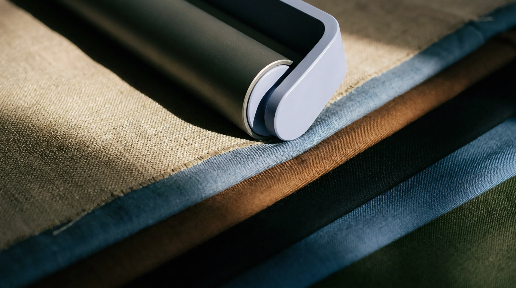 A handheld fabric roller rests diagonally across stacked textile swatches comprising various weave textures and natural yarn hues.